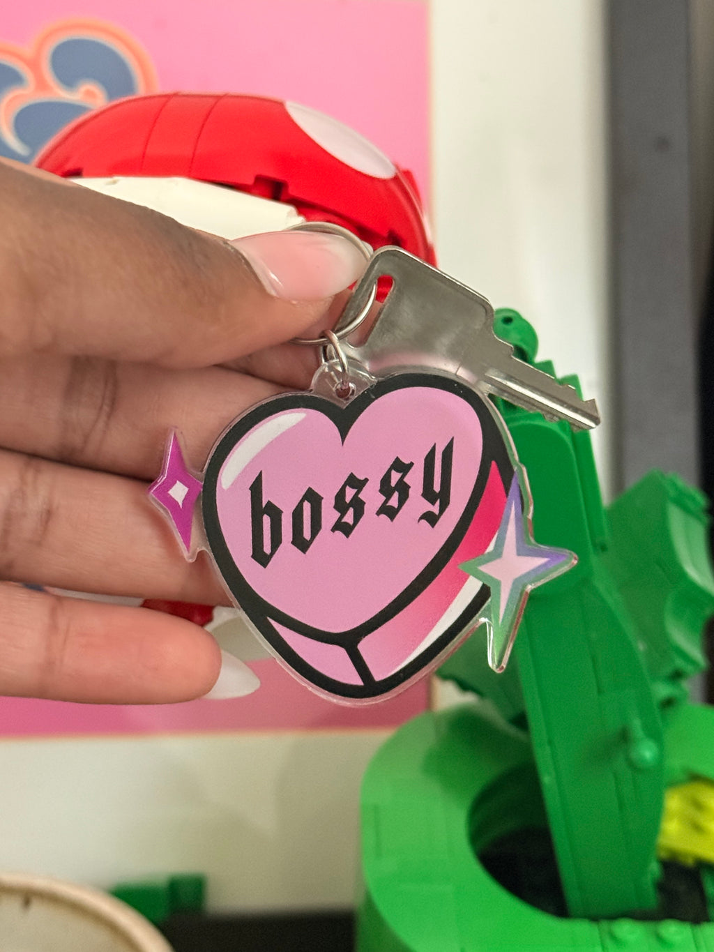 Keychain with pink heart-shaped tag and 'BOSSY' text held by a hand, with colorful background